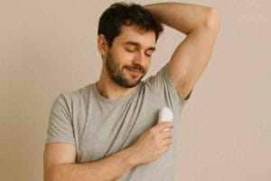 Mies laittaa deodoranttia kainaloon harmaassa t-paidassa