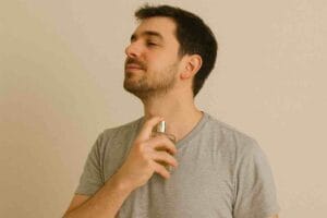 Mies suihkuttaa hajuvettä kaulaansa harmaassa t-paidassa.